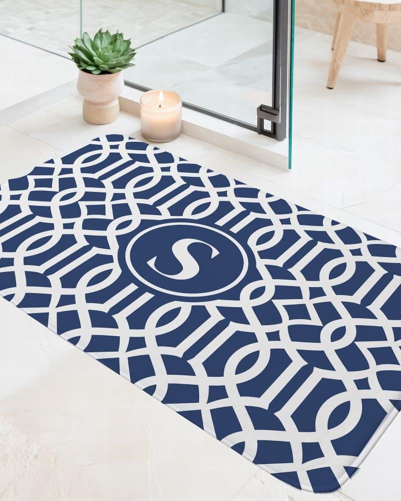 Navy blue bath mat with a white geometric pattern and a centered monogram of the letter S.
