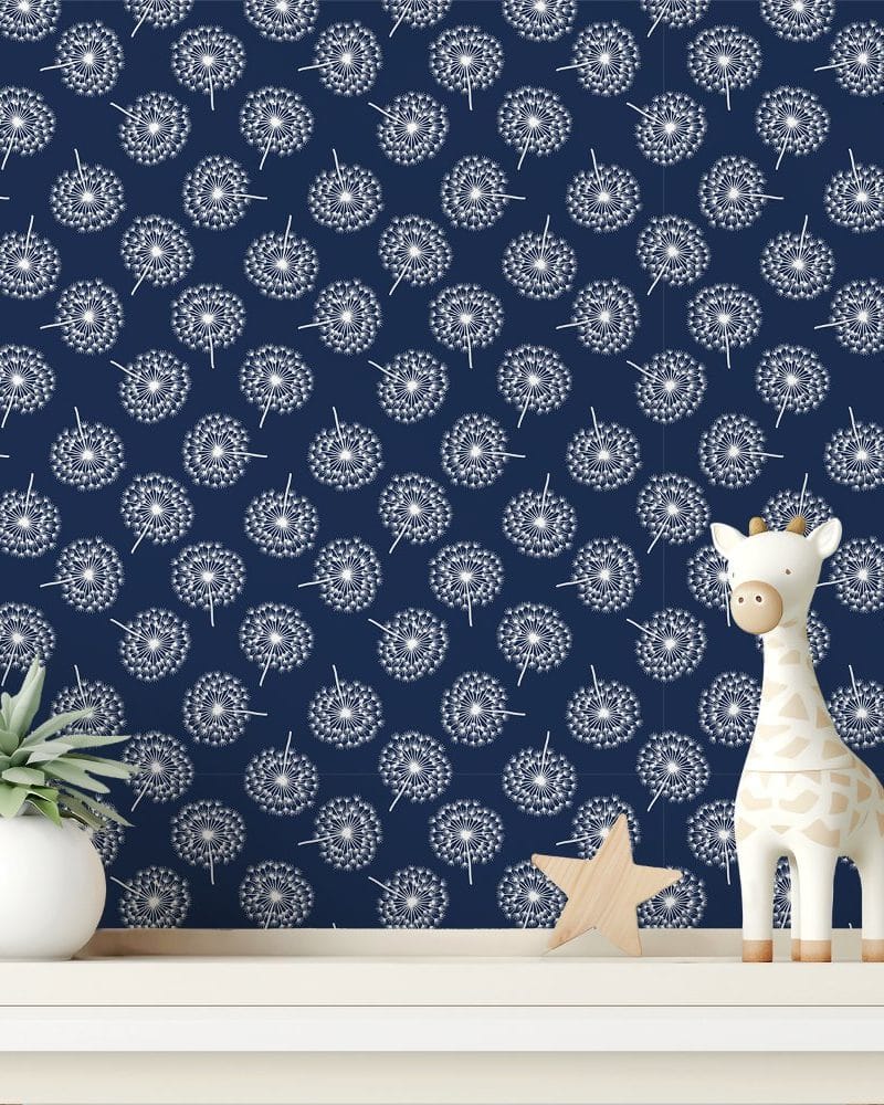 A shelf displays a white giraffe toy and a small potted plant in front of a dark blue wall featuring a repeating pattern of white dandelions.