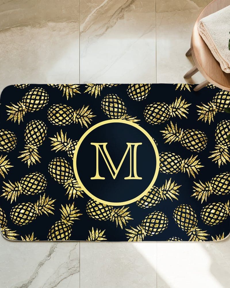 Gold glitter pineapples on a navy blue bath mat with a gold monogram M in the center.