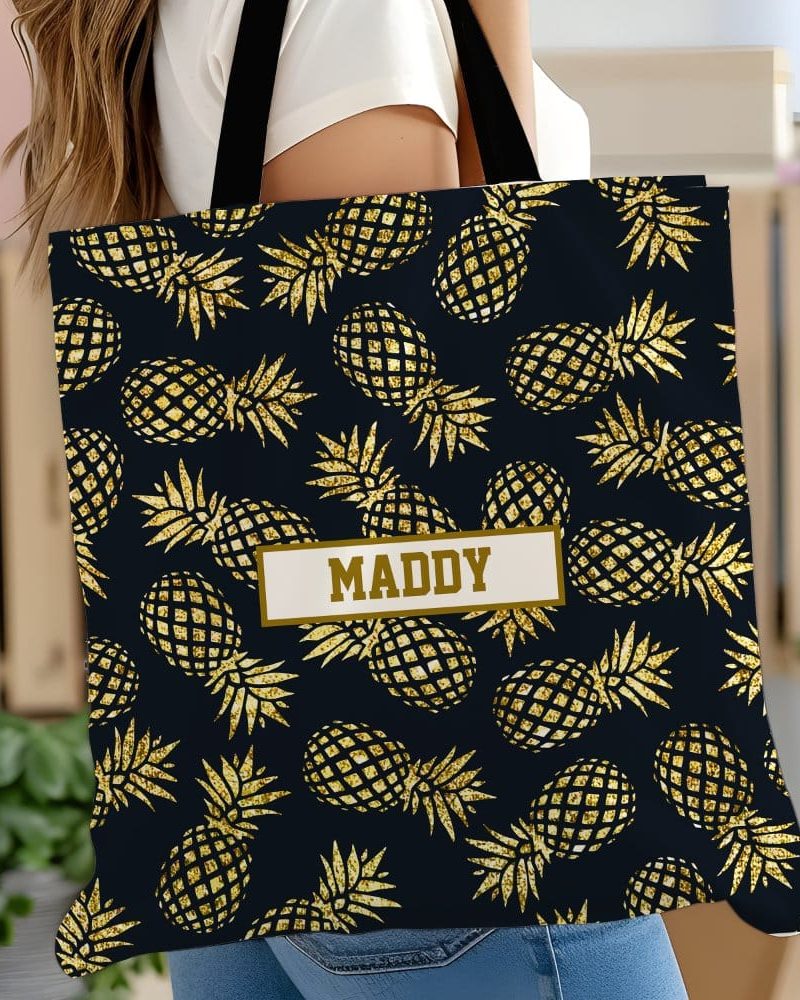 A black tote bag with a gold glitter pineapple pattern and the name Maddy.