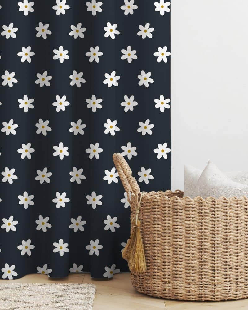 Dark navy blue curtain with a repeating pattern of white daisies, next to a wicker basket containing white pillows.