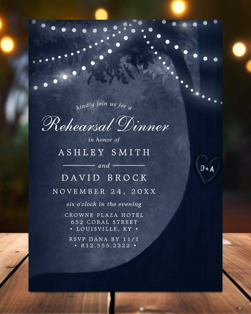 Navy blue rehearsal dinner invitation with a tree silhouette, string lights, and the couple's names.