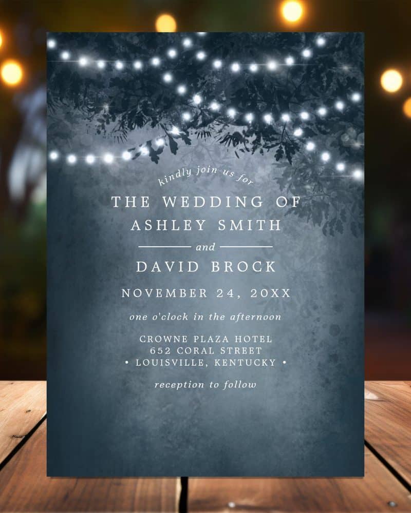 Wedding invitation with a dark blue background featuring string lights hanging from tree branches. The invitation announces the wedding of Ashley Smith and David Brock.