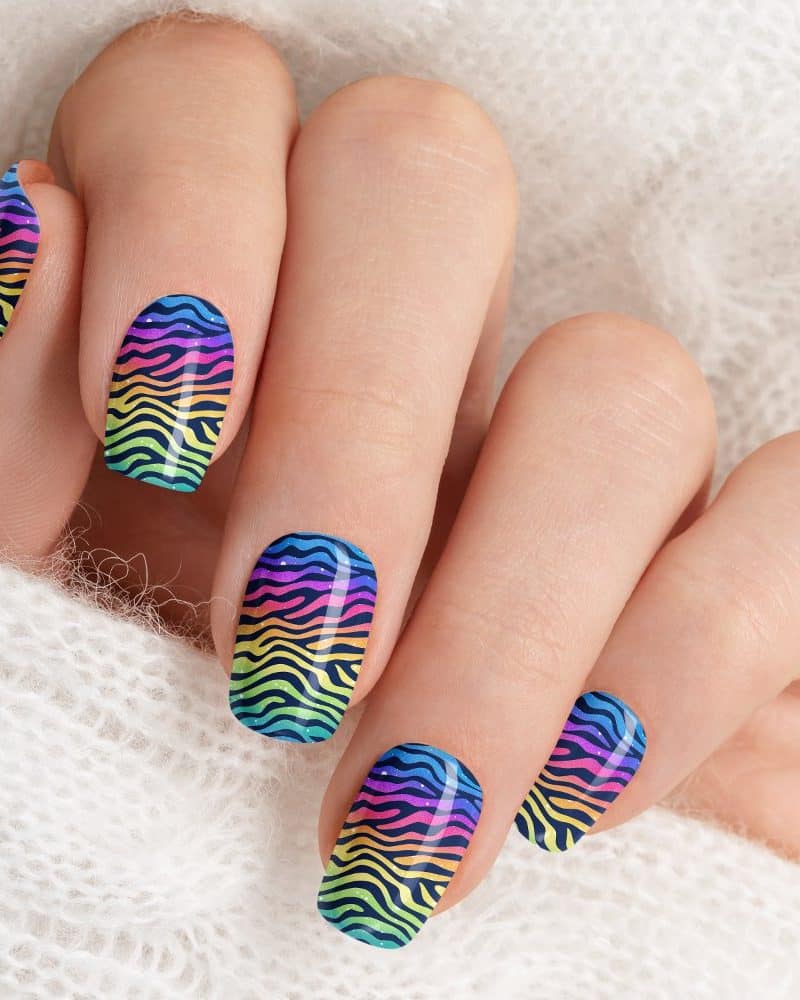 Closeup of a hand with fingernails painted with a rainbow zebra stripe design.