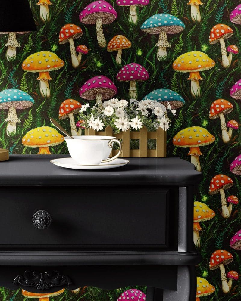 A teacup and saucer sit on a dark-colored nightstand against a backdrop of vibrant mushroom wallpaper.