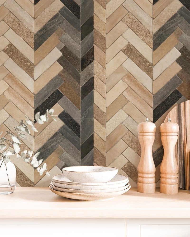 Stack of dishes and kitchen accessories in front of a herringbone patterned backsplash.