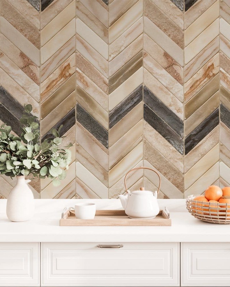 White kitchen counter with a chevron patterned backsplash in beige and gray tones, featuring a teapot, mug, and bowl of oranges.