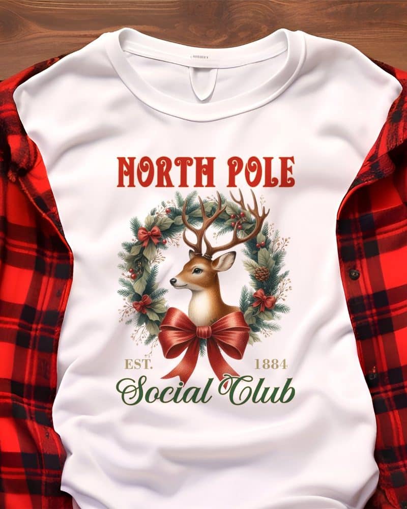 White sweatshirt with a Christmas design featuring a deer in a wreath, text reading North Pole Social Club Est. 1884.