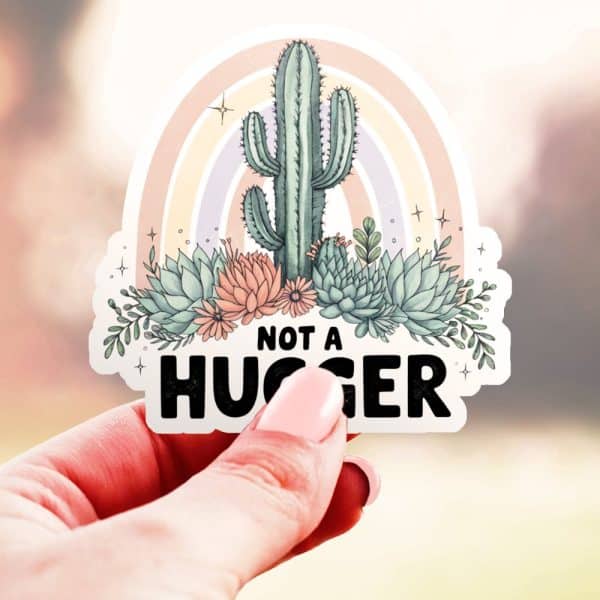 Hand Holding A Sticker Featuring A Cactus And Succulents With A Rainbow Arc Behind Them, And The Text Not A Hugger.