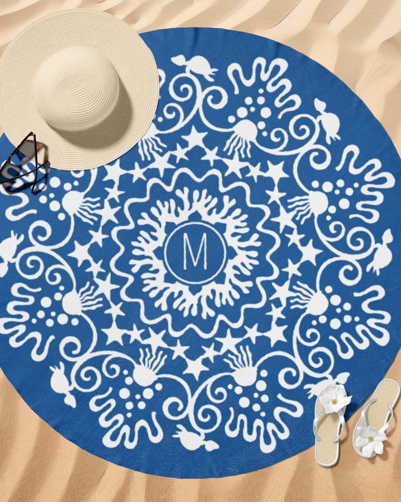 A blue round beach towel with a white mandala design and a central monogram.