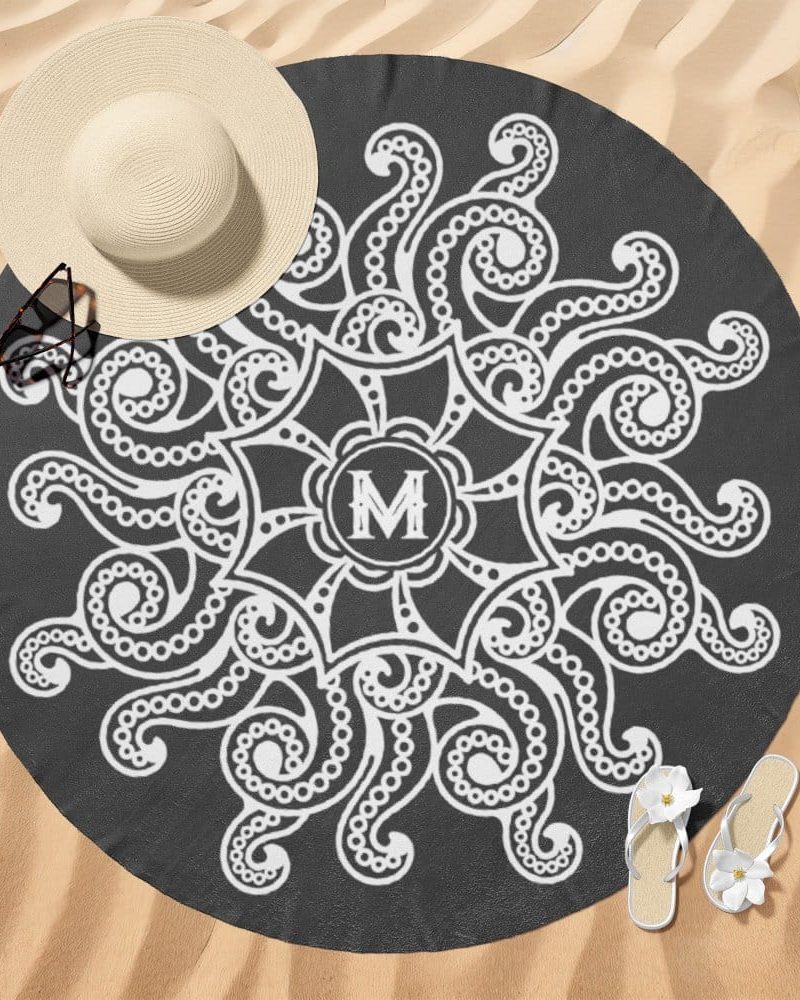 Dark gray round beach towel with a white mandala design featuring the letter M in the center.