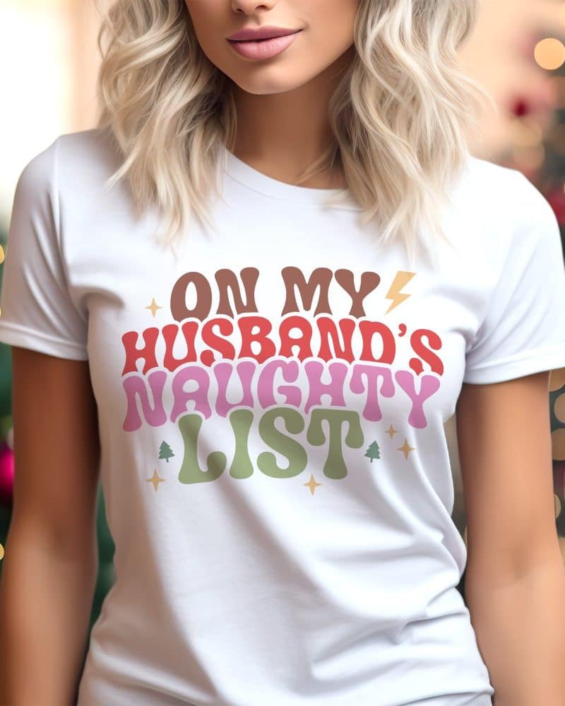 Woman wearing a white t-shirt with a Christmas design that says On My Husband's Naughty List.