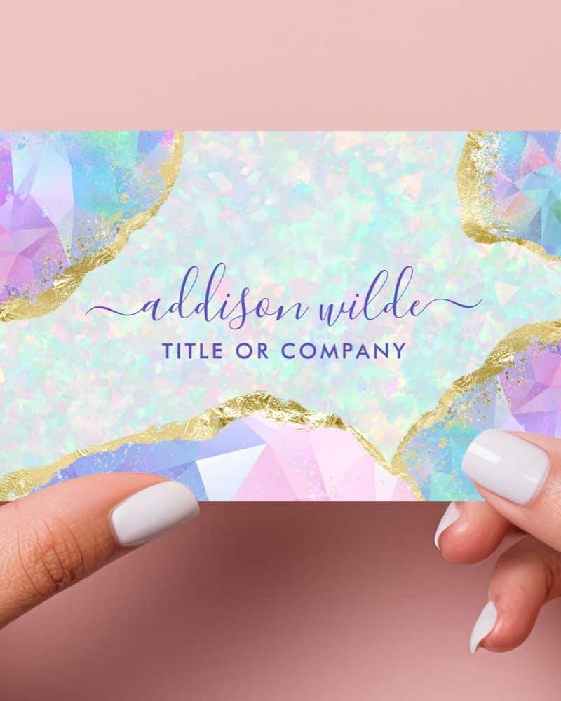 Two hands hold up a pastel business card with gold accents. The card features a design of iridescent gemstones. The name Addison Wilde is printed on the card.
