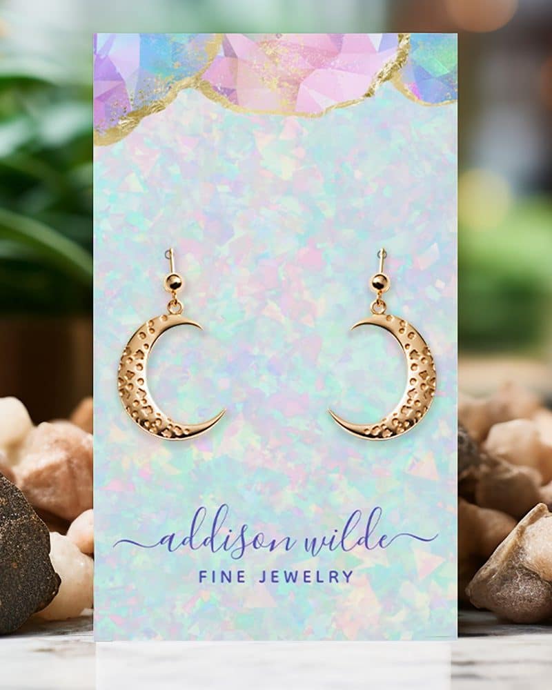 Gold crescent moon earrings displayed on a pastel card.