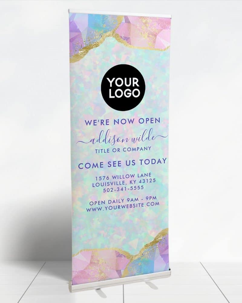 A pastel-colored retractable banner announcing a new business opening. The banner features a pastel and gold geometric design and includes the business name, address, phone number, and website.
