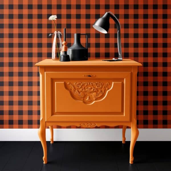 Orange Painted Wooden Cabinet With Ornate Detailing, Against A Black And Orange Gingham Wall.