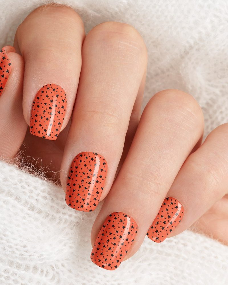 Close up of a hand with orange nails decorated with small black stars.
