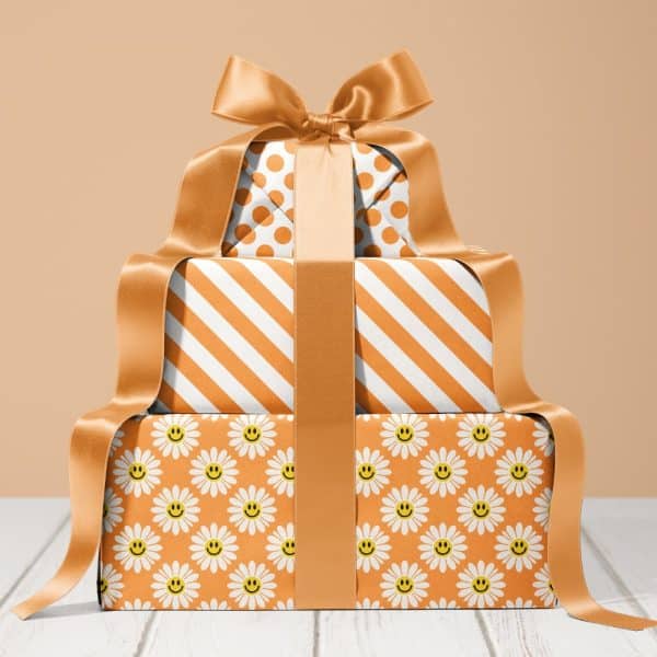 Stack Of Three Gifts Wrapped In Orange Paper With Different Patterns, Tied With A Large Gold Ribbon.