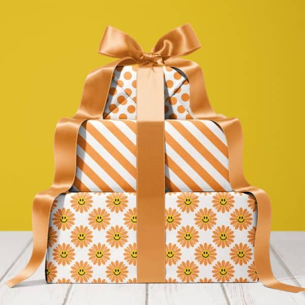 Stack Of Three Gifts Wrapped In Orange And White Patterned Paper With A Large Gold Ribbon.