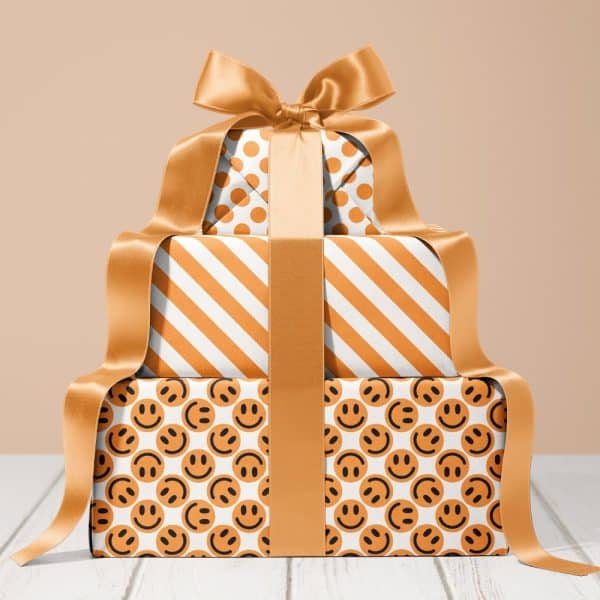 Stack Of Three Gifts Wrapped In Orange And White Patterned Paper With A Large Gold Ribbon.