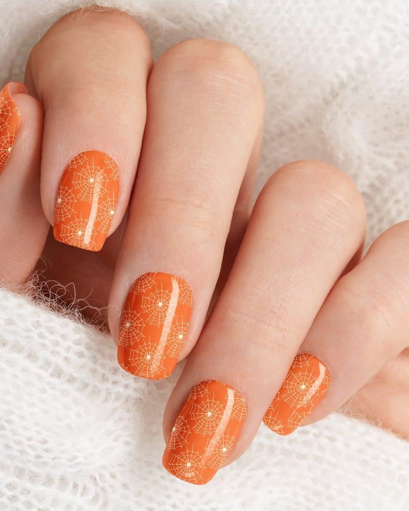A hand with orange nails decorated with white spiderwebs.
