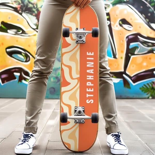Person Holding A Personalized Orange And Beige Skateboard With The Name Stephanie On It.