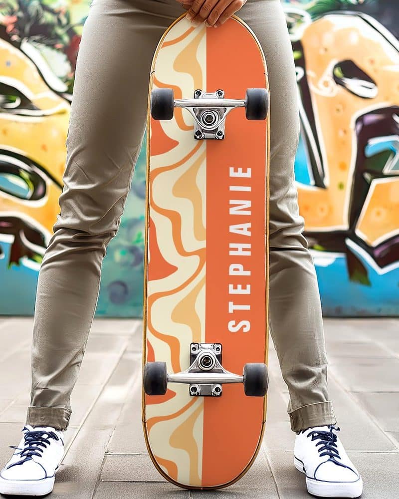 Person holding a personalized orange and beige skateboard with the name Stephanie on it.
