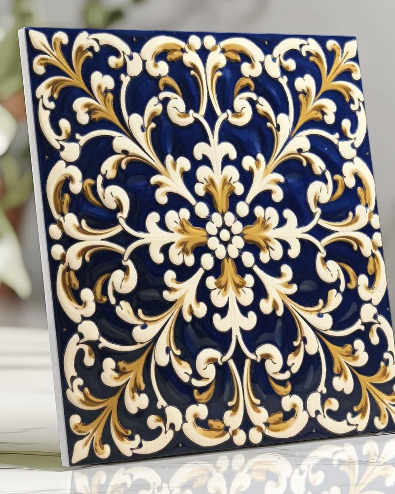 A square tile with an ornate, blue and gold, floral design.