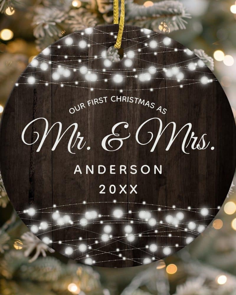 Round Christmas ornament with dark wood background, string lights, and the text Our First Christmas as Mr. & Mrs. Anderson 20XX.