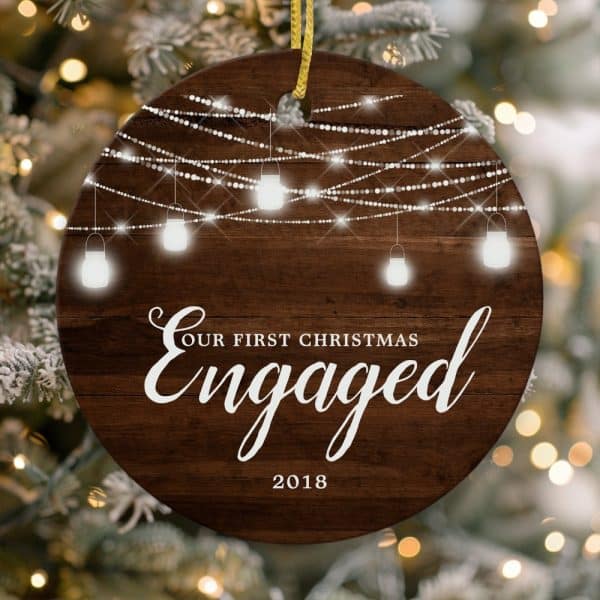 Round Wooden Christmas Ornament With String Lights And The Text Our First Christmas Engaged 2018.