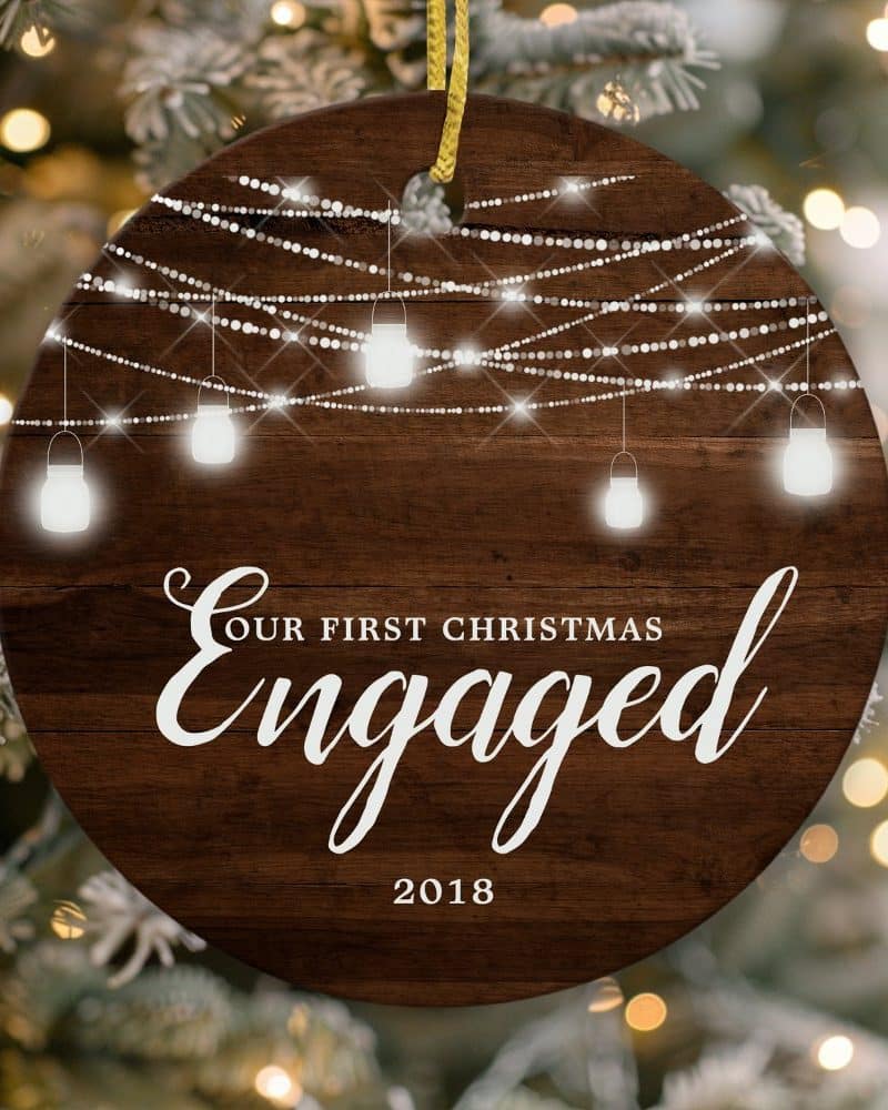 Round wooden Christmas ornament with string lights and the text Our First Christmas Engaged 2018.