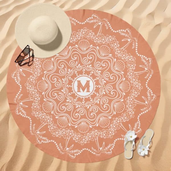 Round Peach-Colored Beach Towel With A White Mandala Design Featuring Seashells, Flowers, And Palm Trees; A Monogrammed M Is In The Center.