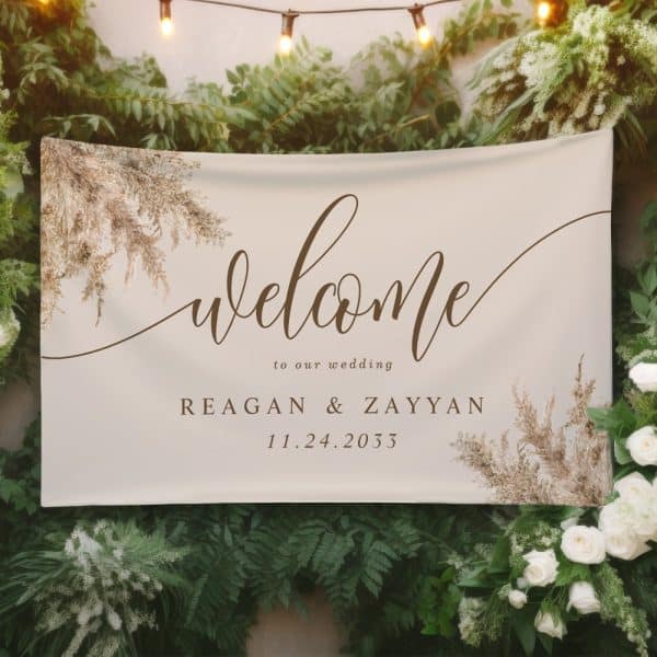 Beige Wedding Welcome Sign With Brown Calligraphy. The Sign Includes The Couple'S Names, Reagan &Amp; Zayyan, And The Wedding Date. Dried Floral Design Accents The Corners.