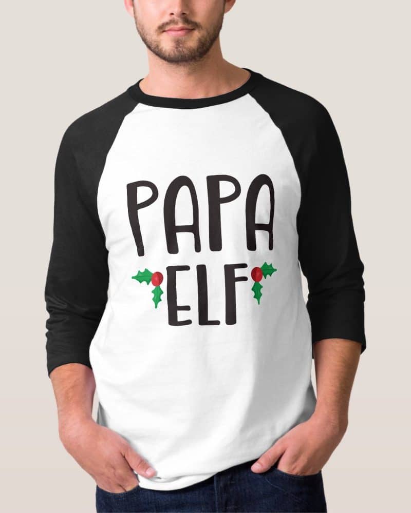 Man wearing a white and black baseball tee that says Papa Elf with holly berries.