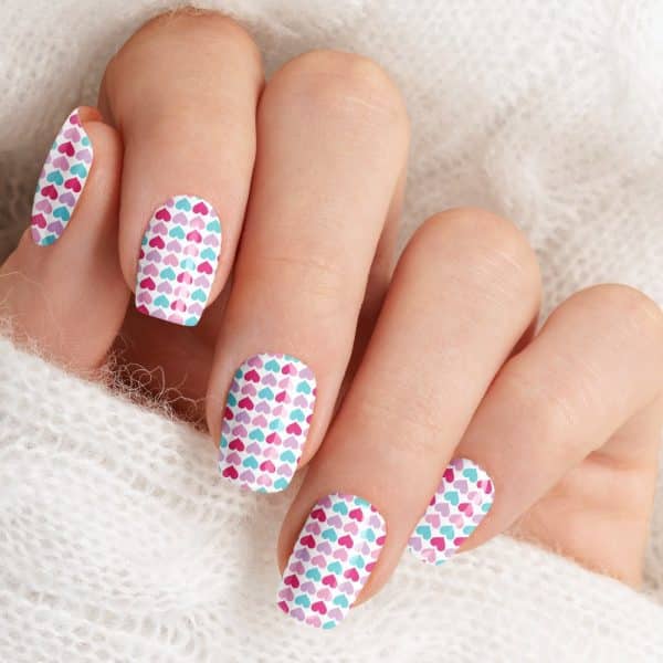 Close-Up Of A Hand With Fingernails Decorated With A Small Heart Pattern In Pink, Purple, And Teal.