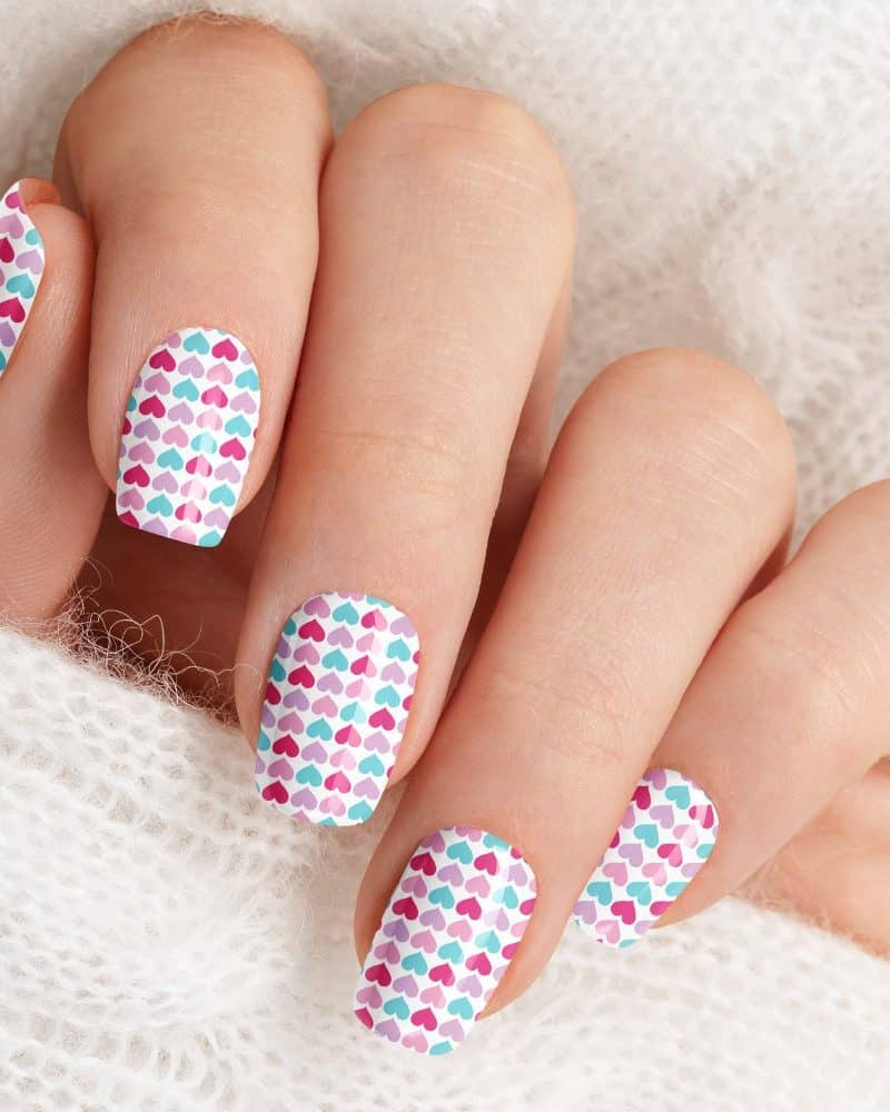Close-up of a hand with fingernails decorated with a small heart pattern in pink, purple, and teal.