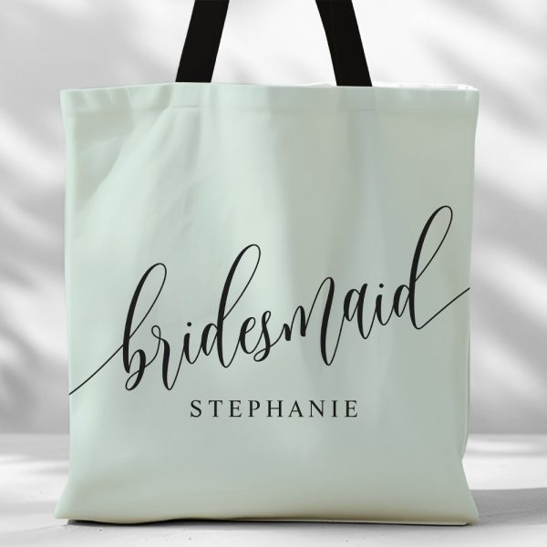 Light Green Tote Bag With Black Handles And The Word Bridesmaid In Elegant Script, Followed By The Name Stephanie.