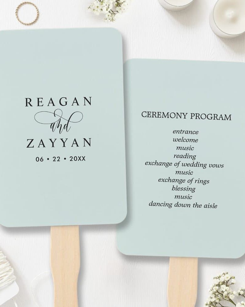 Two light blue wedding ceremony programs attached to wooden handles. One program displays the names Reagan and Zayyan and the wedding date. The other lists the ceremony events.