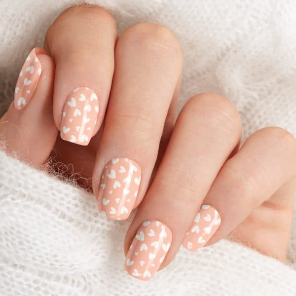 Close-Up Of A Hand With Peach-Colored Nails Decorated With Small White Hearts.