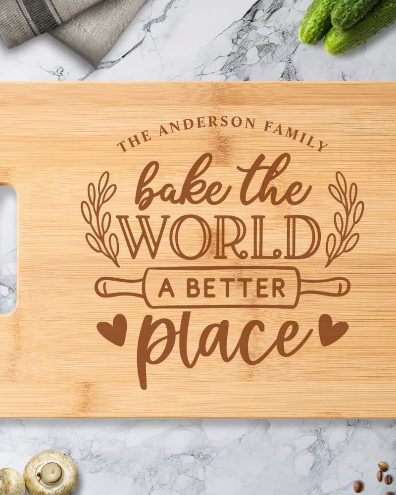 Light brown bamboo cutting board with a handle, engraved with the text Bake the World a Better Place, along with the words The Anderson Family.