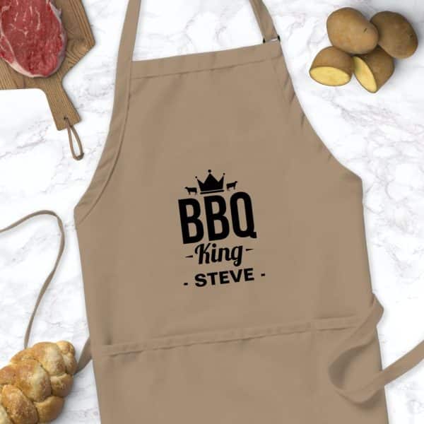 Tan Apron With Black Text Reading Bbq King Steve, And A Crown Graphic Above.