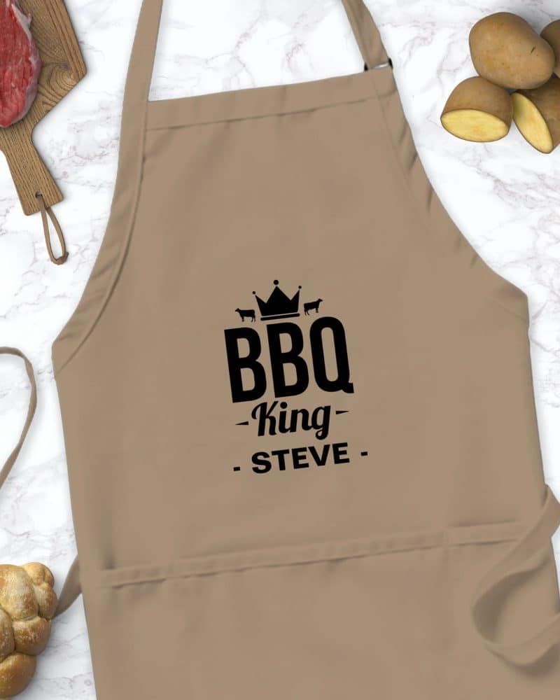Tan apron with black text reading BBQ King Steve, and a crown graphic above.