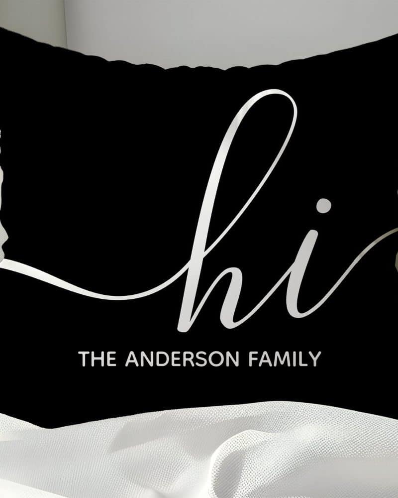 Black pillow with white cursive "hi" and "The Anderson Family" below.