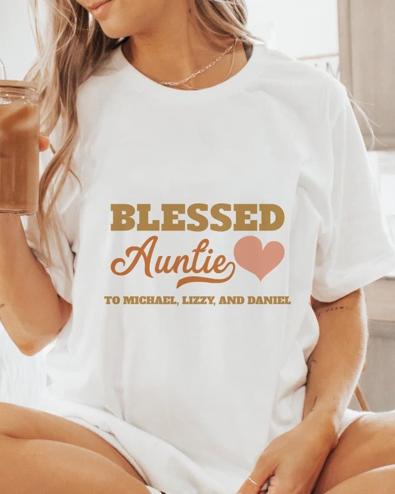 Woman wearing a white t-shirt that says Blessed Auntie with a heart and the names Michael, Lizzy, and Daniel.