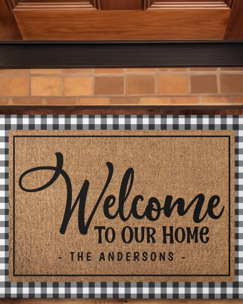 A welcome mat with a black and white buffalo check border. The mat says Welcome to Our Home, The Andersons.