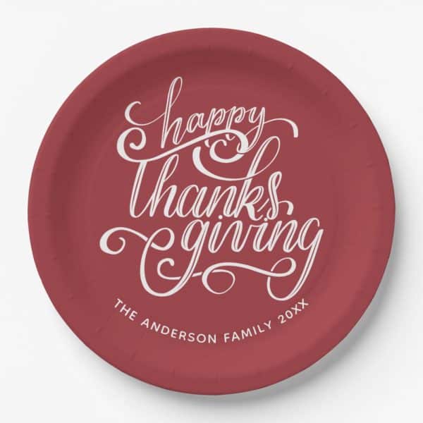 A Maroon Paper Plate With White Cursive Lettering That Says Happy Thanksgiving And The Anderson Family 20Xx.
