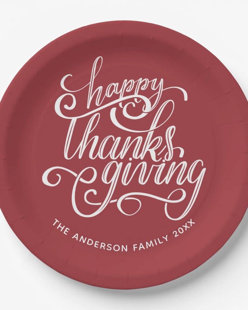 A maroon paper plate with white cursive lettering that says Happy Thanksgiving and The Anderson Family 20XX.
