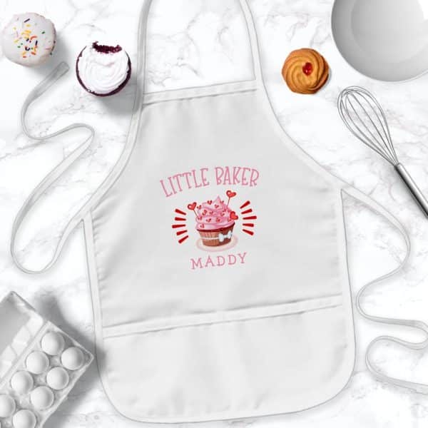 White Child'S Apron With Pink Cupcake Design And The Name Maddy.