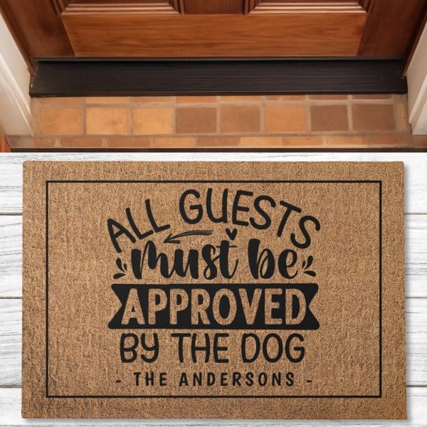 A Tan Coir Doormat With Black Text That Reads All Guests Must Be Approved By The Dog, And The Name The Andersons.
