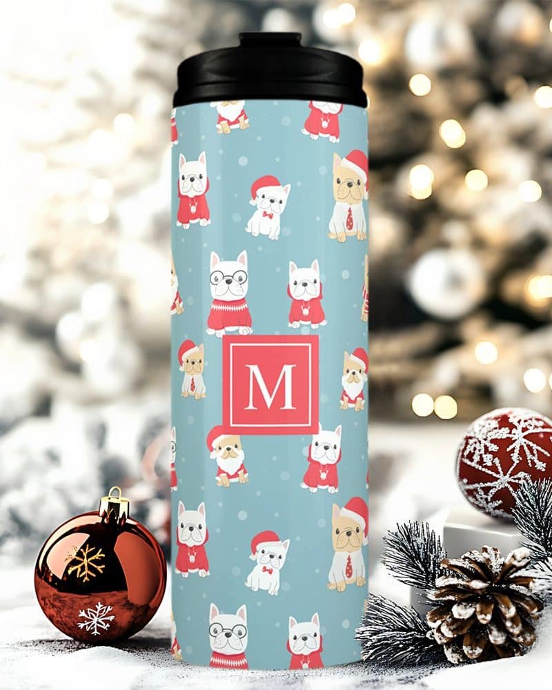 A travel mug with a Christmas design featuring French bulldogs wearing Santa hats and sweaters. The mug is personalized with the letter M.